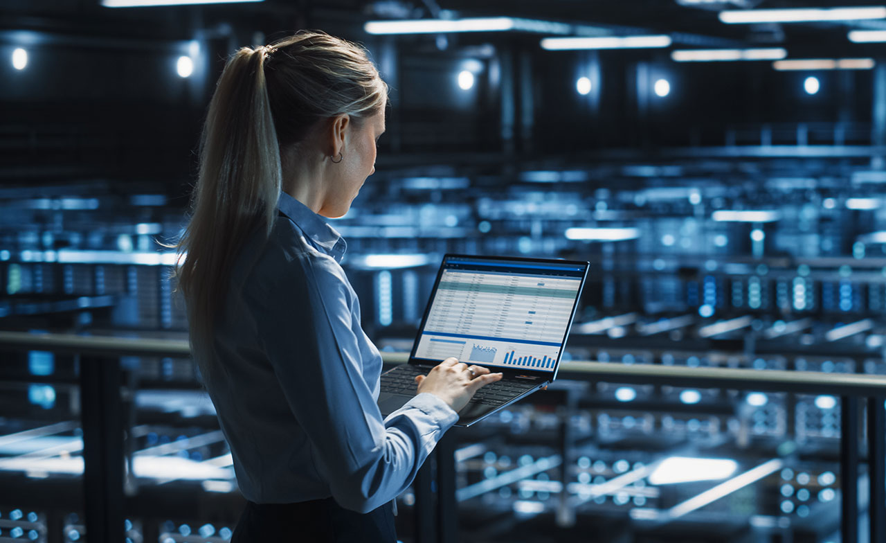Consultant reviewing CGI SiteReliability360 on a laptop overlooking a server room