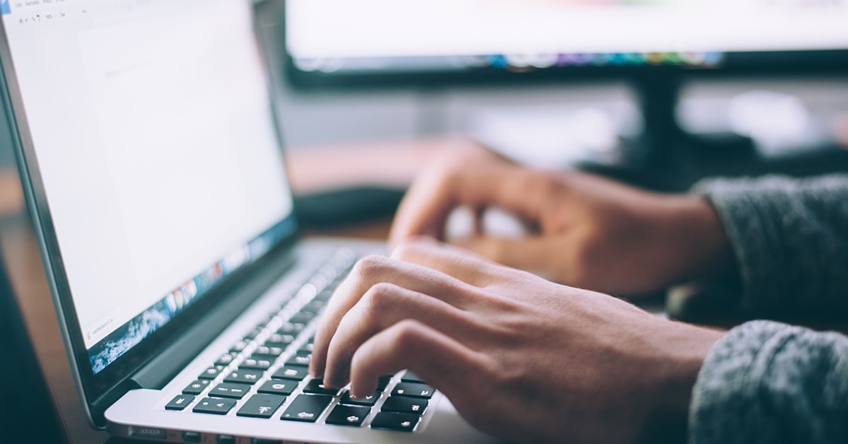 Händerna på en man som sitter och knappar på en laptops tangentbord.