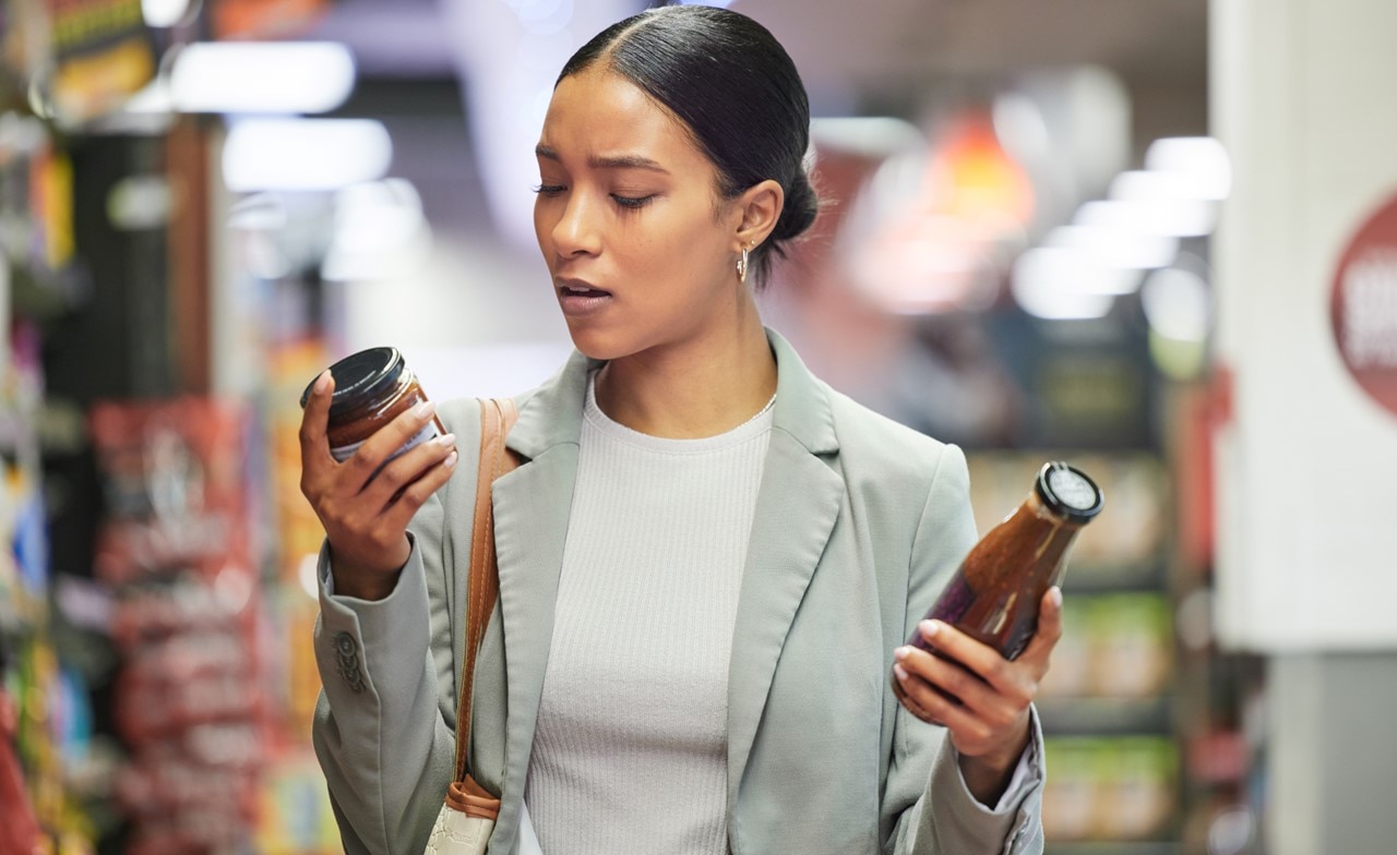 customer in supermarket reading product labels to compare sauce bottles