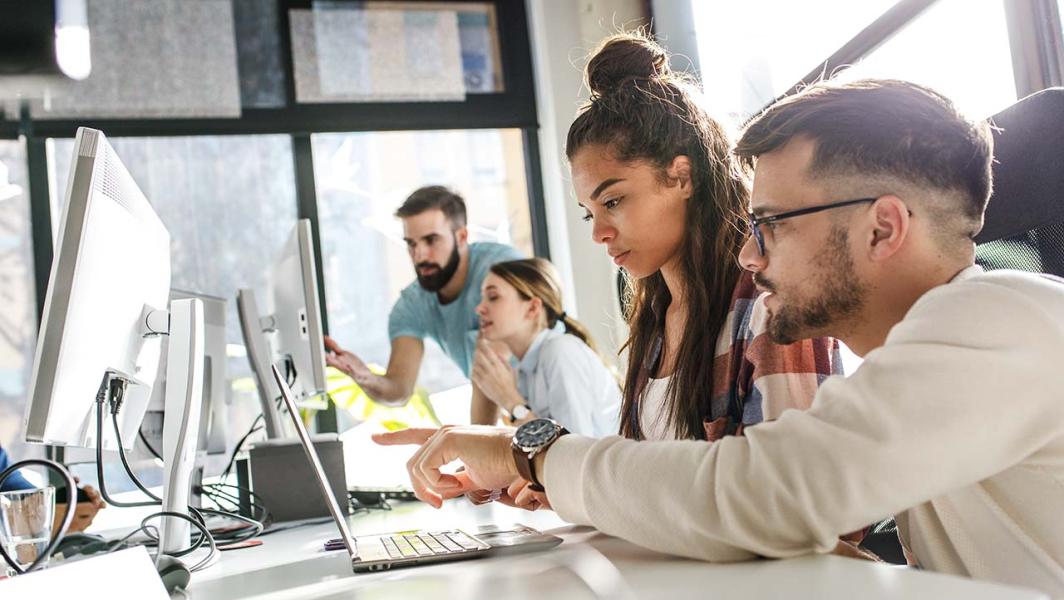 Co-workers working and talking in front of computer screens 