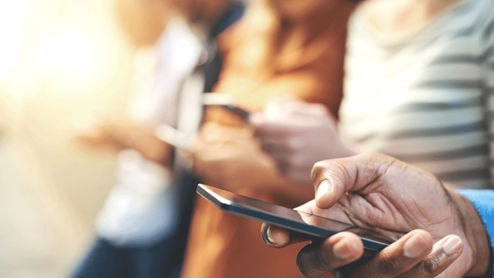 Man’s hand holding a mobile phone with other people in the background