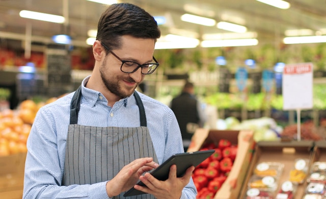 Verkäufer steht in der Obstabteilung und kontrolliert den Warenbestand per Tablet
