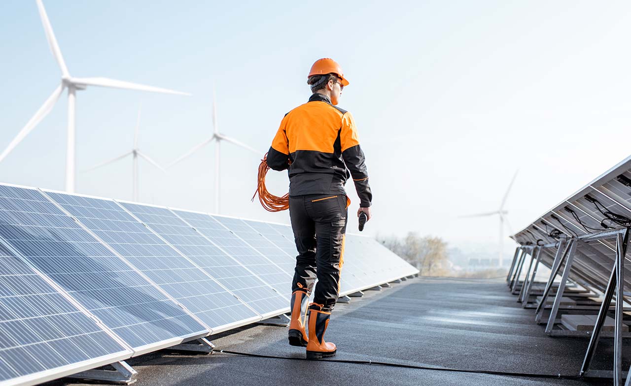 Person walking along solar panels with windmills in the distance