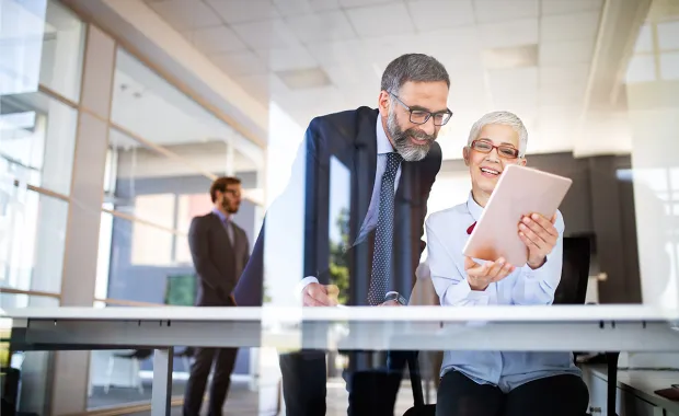 Zwei Kollegen in einer Bank freuen sich über den erfolgreichen KI-gestützten Onboarding-Prozess auf einem Tablet