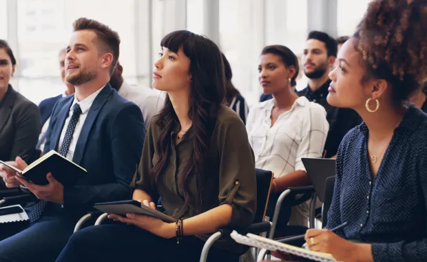 Training session with audience of professionals sitting in chairs holding notebooks