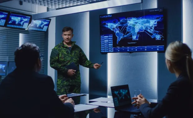Military personnel meeting in front of monitors and a laptop